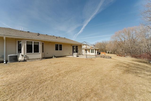 back of property with central air condition unit, a lawn, a shingled roof, and a patio