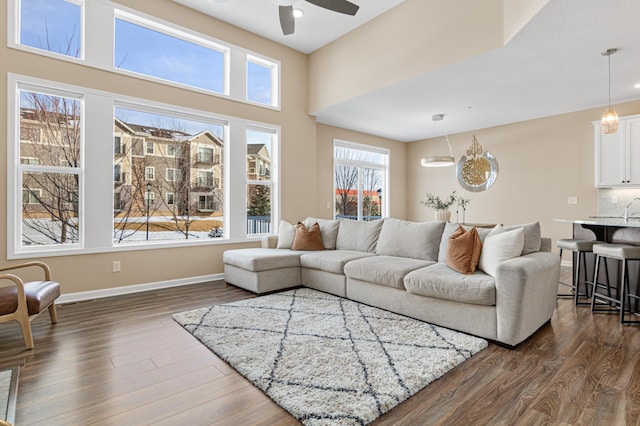 living area featuring ceiling fan, dark wood-style flooring, a towering ceiling, and baseboards