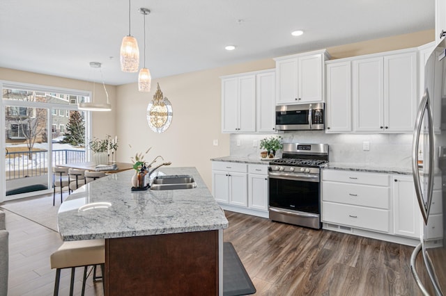 kitchen featuring a breakfast bar area, a sink, appliances with stainless steel finishes, backsplash, and dark wood finished floors