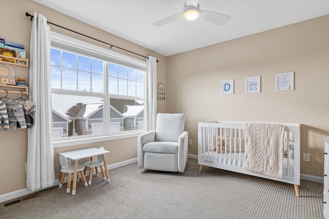 bedroom featuring a crib, baseboards, visible vents, a ceiling fan, and carpet flooring