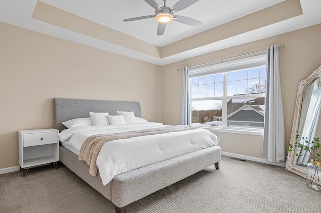 carpeted bedroom with ceiling fan, a tray ceiling, visible vents, and baseboards