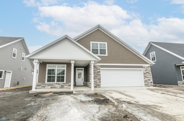 view of front facade with stone siding, a porch, driveway, and a garage