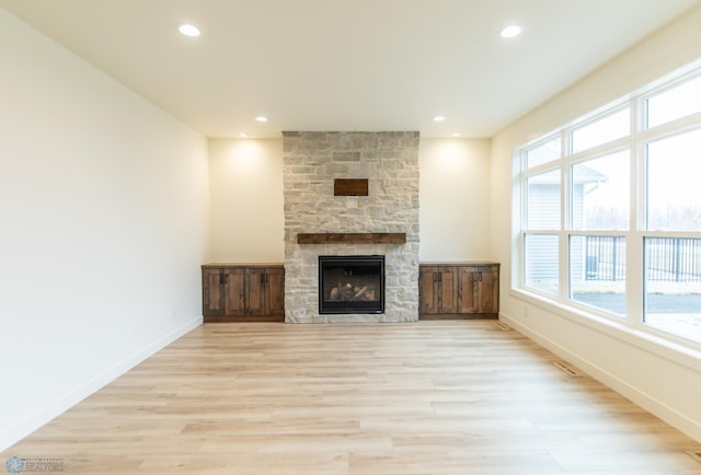 unfurnished living room with a stone fireplace, light wood-style flooring, visible vents, and baseboards