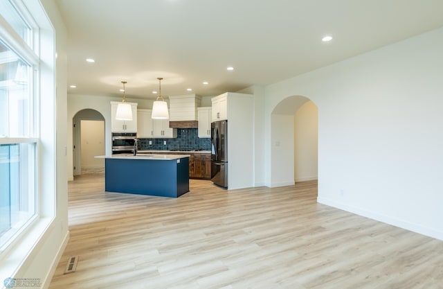 kitchen featuring backsplash, open floor plan, freestanding refrigerator, arched walkways, and stainless steel oven