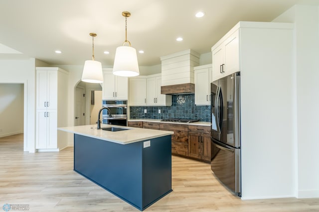 kitchen featuring an island with sink, a sink, tasteful backsplash, stainless steel appliances, and light countertops