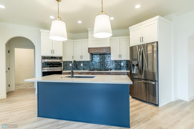 kitchen featuring a sink, stainless steel appliances, arched walkways, light wood finished floors, and hanging light fixtures