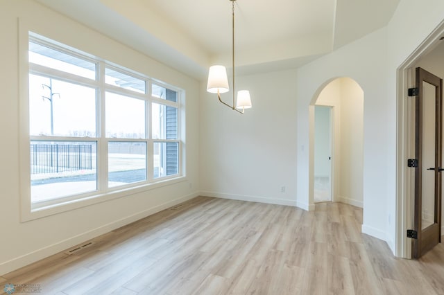 unfurnished room featuring visible vents, light wood-style floors, arched walkways, and baseboards