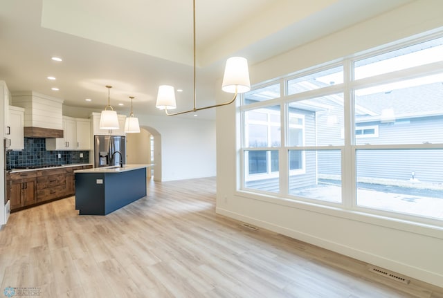 kitchen with decorative backsplash, arched walkways, plenty of natural light, and stainless steel fridge with ice dispenser