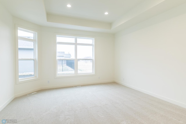 empty room featuring a tray ceiling, visible vents, baseboards, and light colored carpet