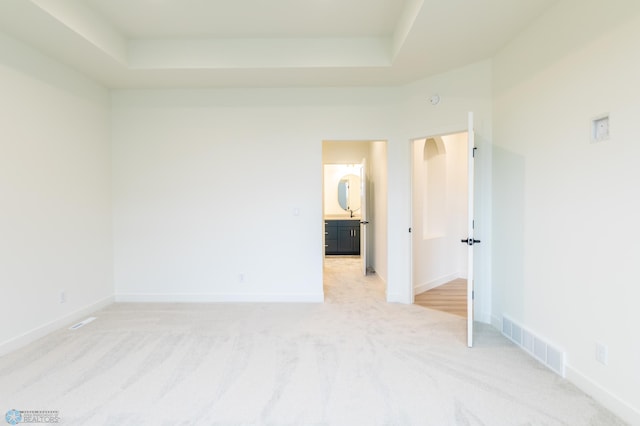 empty room featuring a tray ceiling, visible vents, baseboards, and light colored carpet