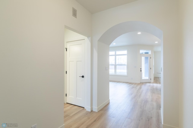 corridor with light wood-type flooring, visible vents, recessed lighting, arched walkways, and baseboards