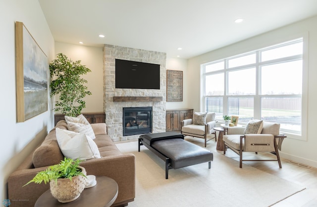 living area with a stone fireplace, light wood-style flooring, recessed lighting, and baseboards