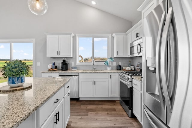 kitchen featuring backsplash, appliances with stainless steel finishes, white cabinetry, a sink, and wood finished floors