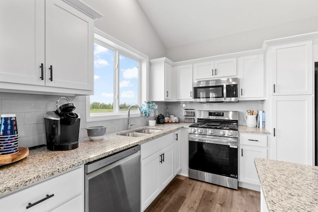 kitchen featuring wood finished floors, a sink, white cabinets, vaulted ceiling, and appliances with stainless steel finishes