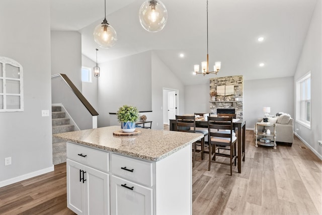 kitchen with white cabinets, a center island, a stone fireplace, light wood-type flooring, and pendant lighting