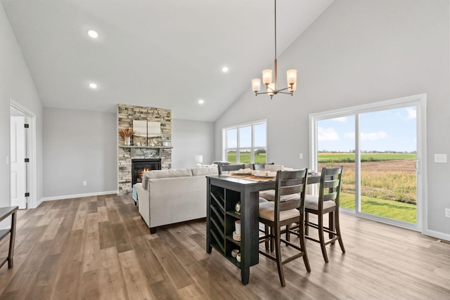 dining area with a notable chandelier, a stone fireplace, wood finished floors, and baseboards