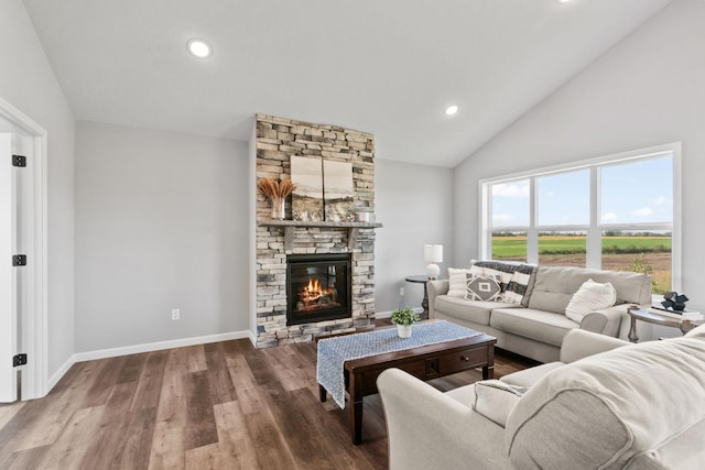 living area featuring baseboards, lofted ceiling, wood finished floors, a stone fireplace, and recessed lighting