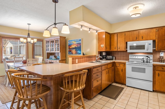 kitchen featuring backsplash, a peninsula, brown cabinetry, white appliances, and a sink