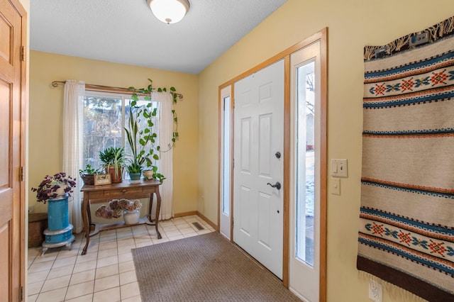 foyer entrance featuring light tile patterned floors, baseboards, visible vents, and a textured ceiling