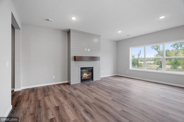 unfurnished living room with a large fireplace, baseboards, wood finished floors, and recessed lighting