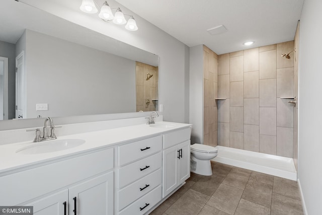 bathroom featuring a tile shower, double vanity, a sink, and toilet