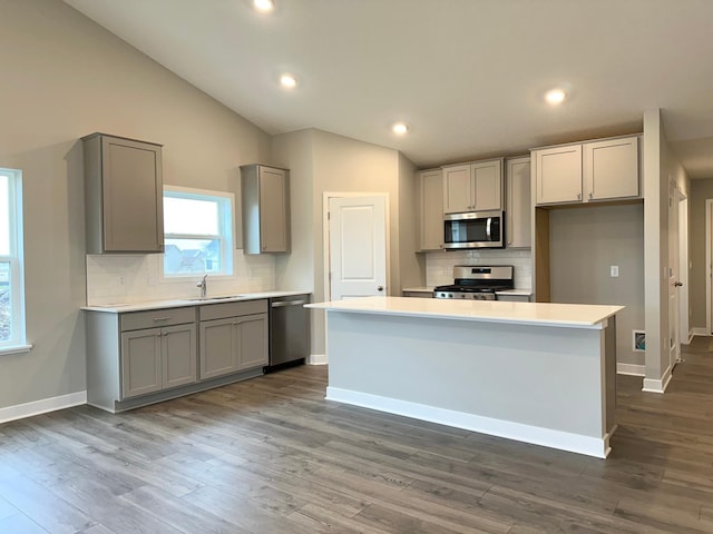 kitchen with stainless steel appliances, vaulted ceiling, a sink, and gray cabinetry