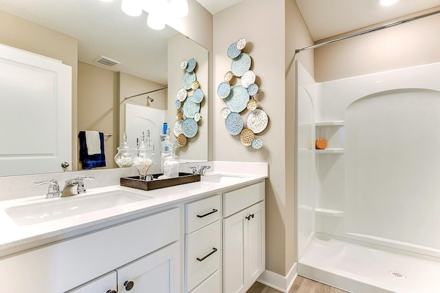 bathroom featuring double vanity, walk in shower, a sink, and visible vents