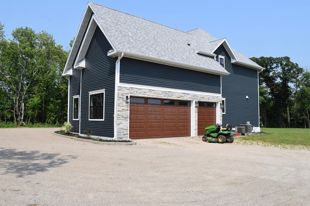 12424 126th Ave NE, Thief River Falls, MN 56701 - view of property exterior featuring a shingled roof, dirt driveway, a garage, stone siding, and cooling unit