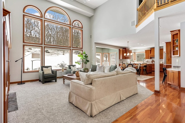 living area featuring baseboards, visible vents, a towering ceiling, light wood-type flooring, and a notable chandelier