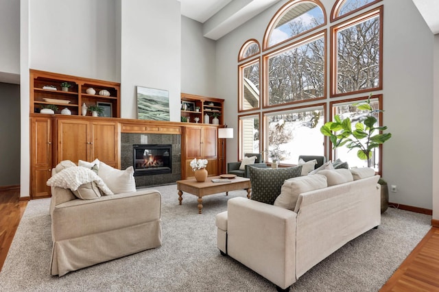 living room featuring a fireplace, wood finished floors, a towering ceiling, and baseboards