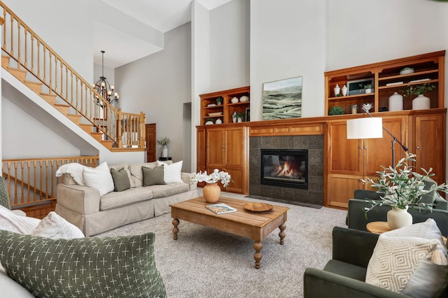 carpeted living area featuring stairway, a tile fireplace, a chandelier, and a towering ceiling