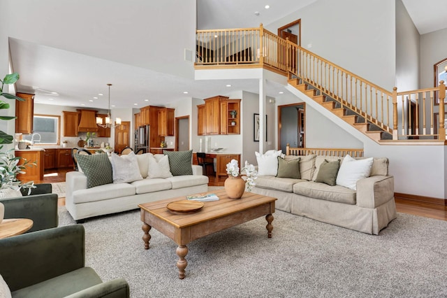 living area featuring recessed lighting, a towering ceiling, light wood-style floors, a chandelier, and stairs