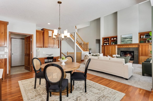 dining space featuring stairs, a tiled fireplace, wood finished floors, and a notable chandelier