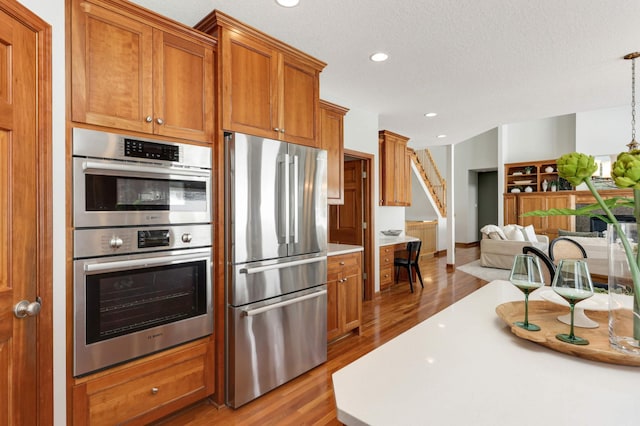 kitchen with brown cabinetry, open floor plan, wood finished floors, light countertops, and stainless steel appliances