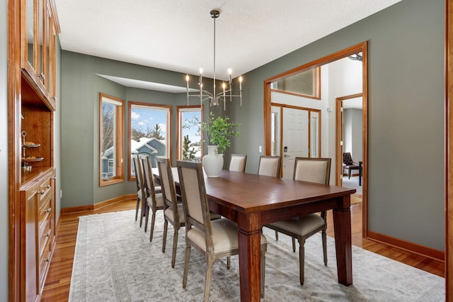 dining area featuring light wood-style floors, a notable chandelier, and baseboards