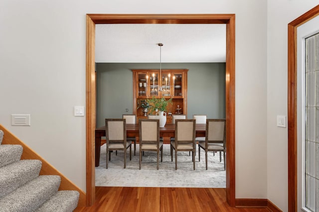 dining room with stairs, a chandelier, wood finished floors, and baseboards