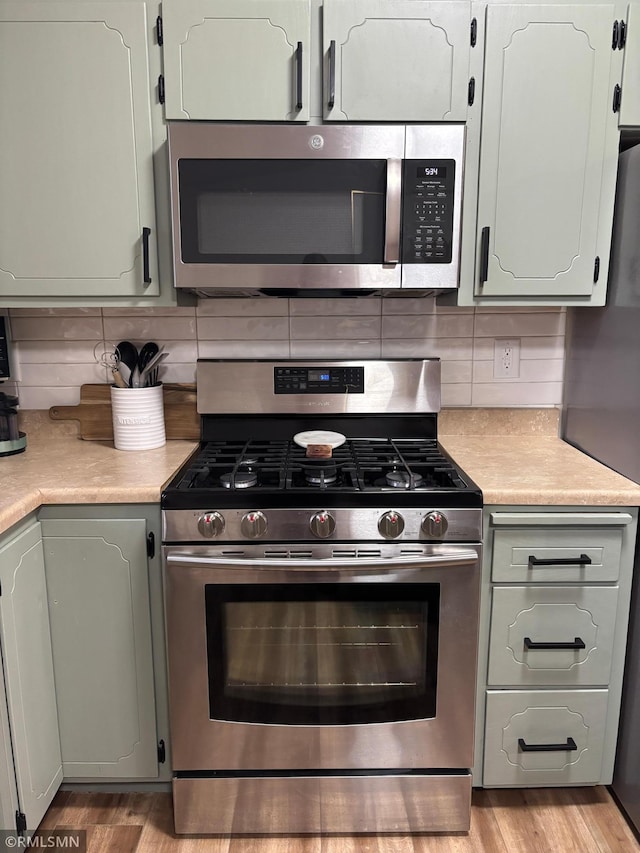 kitchen featuring stainless steel appliances, tasteful backsplash, light wood-type flooring, and light countertops