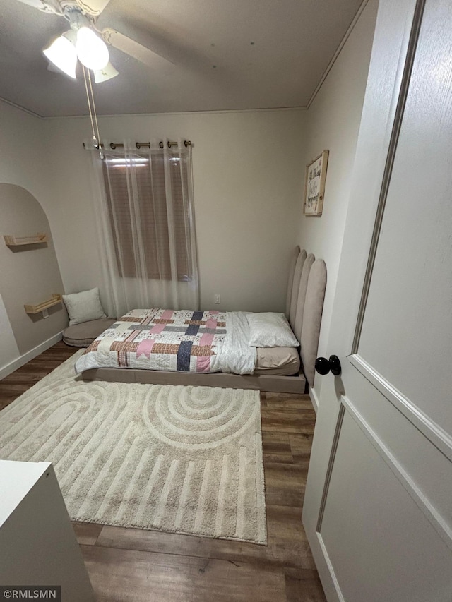 bedroom with arched walkways, ceiling fan, wood finished floors, and baseboards