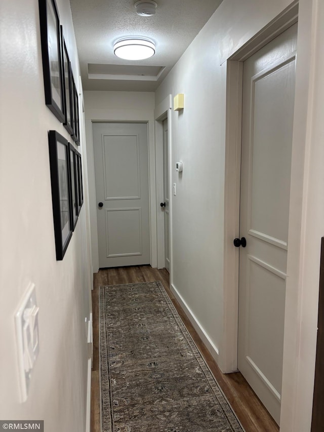 hallway with a textured ceiling, wood finished floors, and baseboards