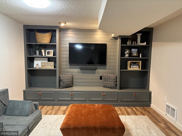 living room with built in shelves, light wood-type flooring, visible vents, and a textured ceiling