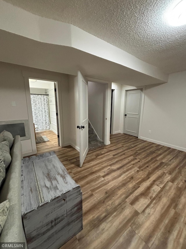 finished below grade area with a textured ceiling, stairway, wood finished floors, and baseboards