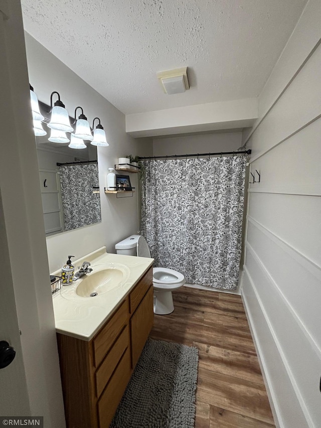 full bathroom with a shower with shower curtain, toilet, wood finished floors, a textured ceiling, and vanity