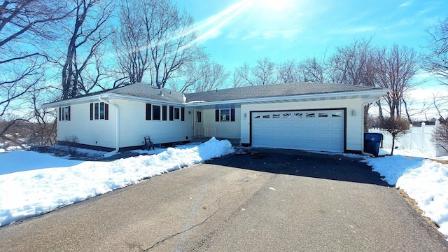 ranch-style home featuring aphalt driveway, a shingled roof, an attached garage, and fence