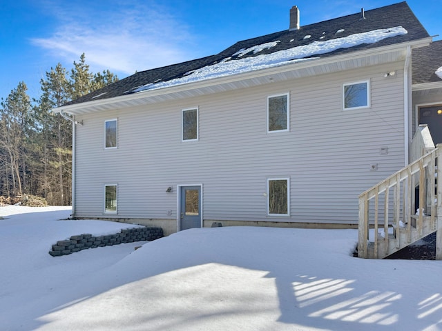 snow covered rear of property with a chimney