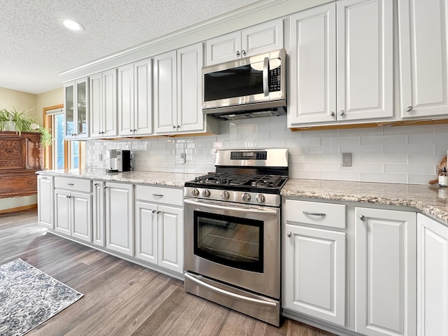 kitchen featuring appliances with stainless steel finishes, white cabinets, glass insert cabinets, and light wood-style flooring