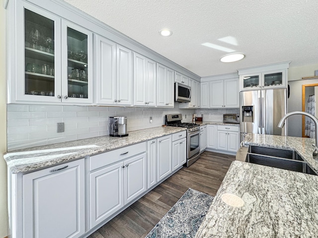 kitchen featuring tasteful backsplash, appliances with stainless steel finishes, dark wood-type flooring, white cabinets, and a sink