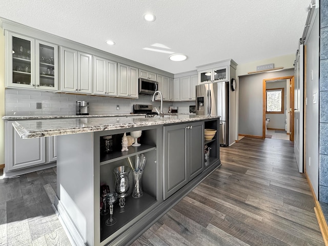 kitchen with gray cabinetry, dark wood-type flooring, appliances with stainless steel finishes, backsplash, and open shelves