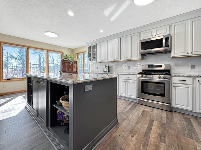 kitchen with a center island, stainless steel appliances, decorative backsplash, a sink, and hardwood / wood-style flooring