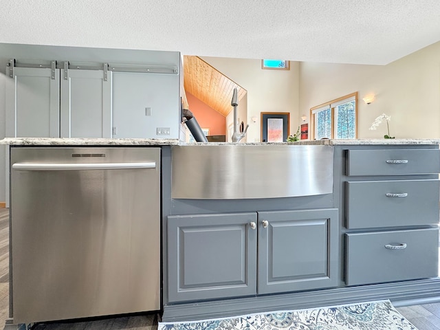 interior space featuring wood finished floors, gray cabinetry, stainless steel dishwasher, a textured ceiling, and light stone countertops