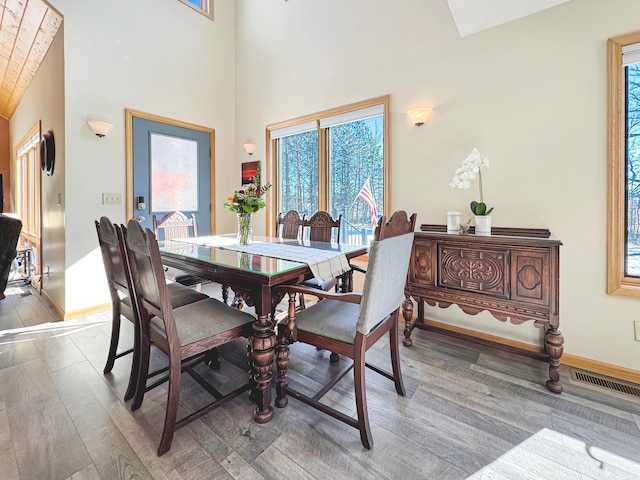 dining area with baseboards, a high ceiling, visible vents, and wood finished floors